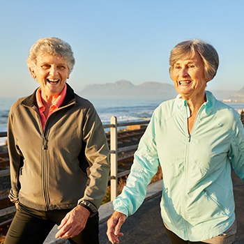  Two women walking with smiles on their faces.